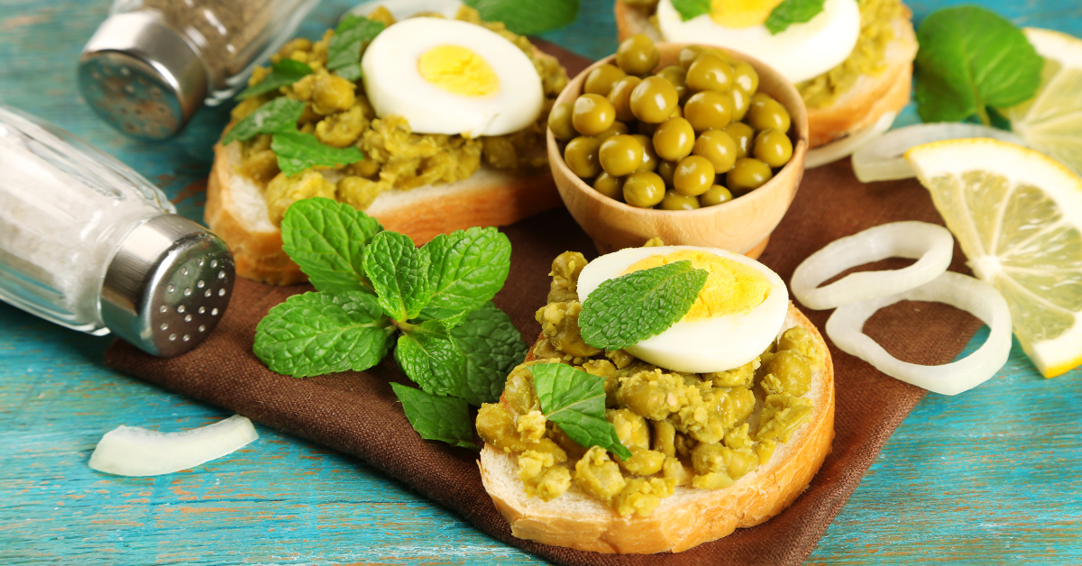 Two sandwiches spread with green pea paste. On each lies a slice of hard-boiled egg. There are spices and mint leaves all around