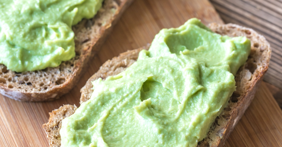 Two slices of bread spread with green avocado paste. The bread is reminiscent of mountain-type