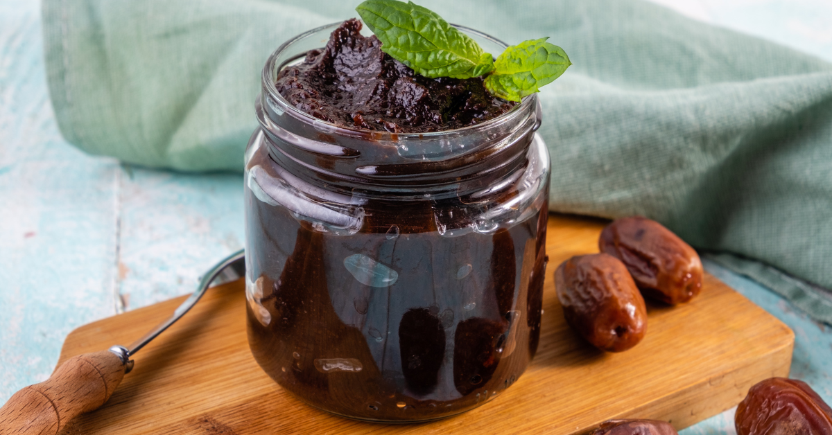 A jar of dark date paste, placed on a wooden board