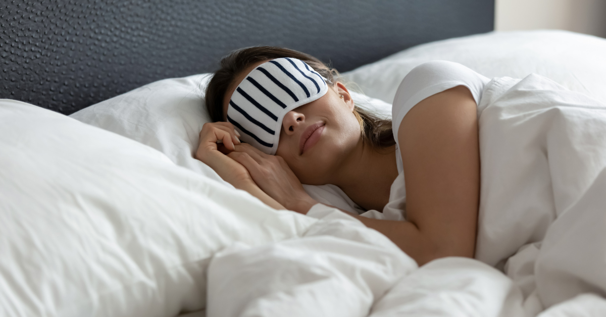 young woman sleeping in white sheets with a blindfold over her eyes