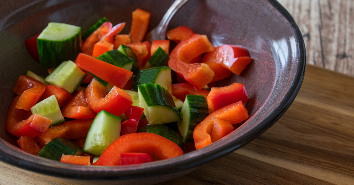 A bowl full of fresh cucumber and red peppers, sprinkled with spices
