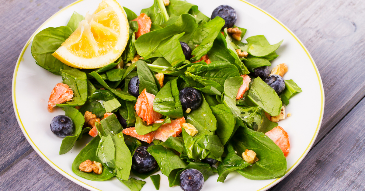 Plate with spinach, blueberries, lemon segments and yam pieces.