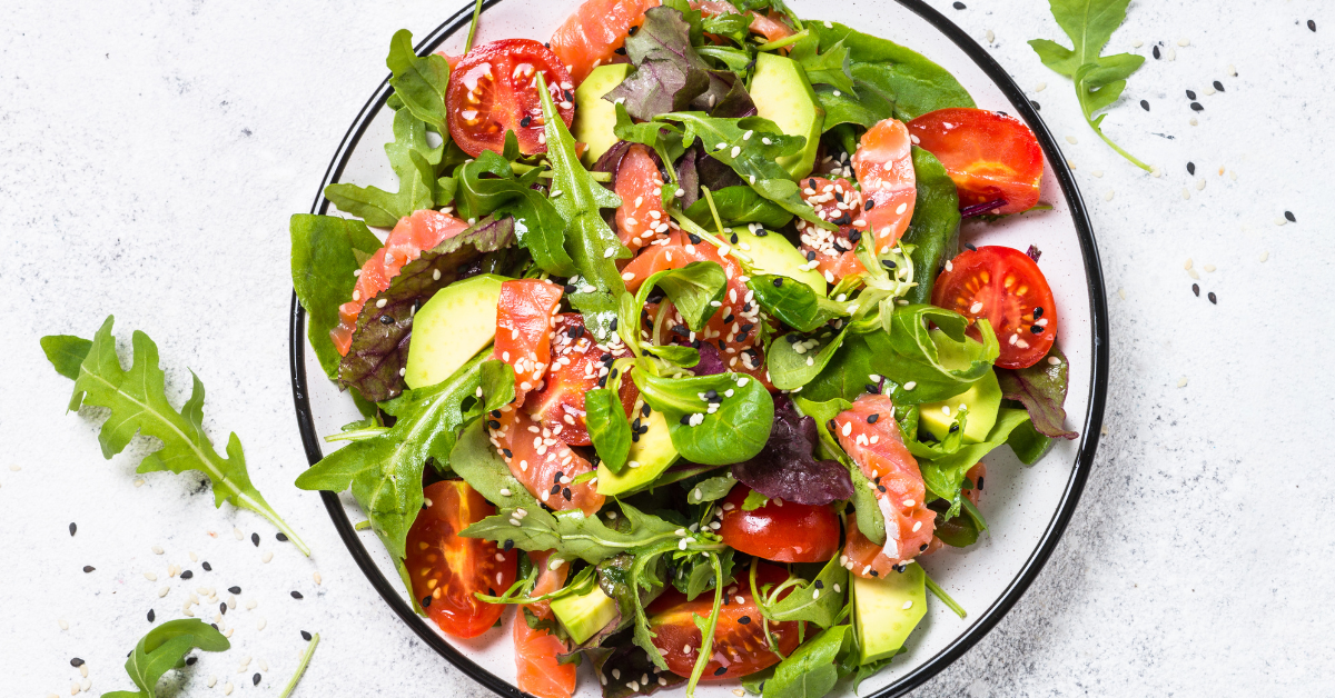 A plate full of ingredients with omega-3 fatty acids such as salmon, cherry tomatoes, mixed salads.