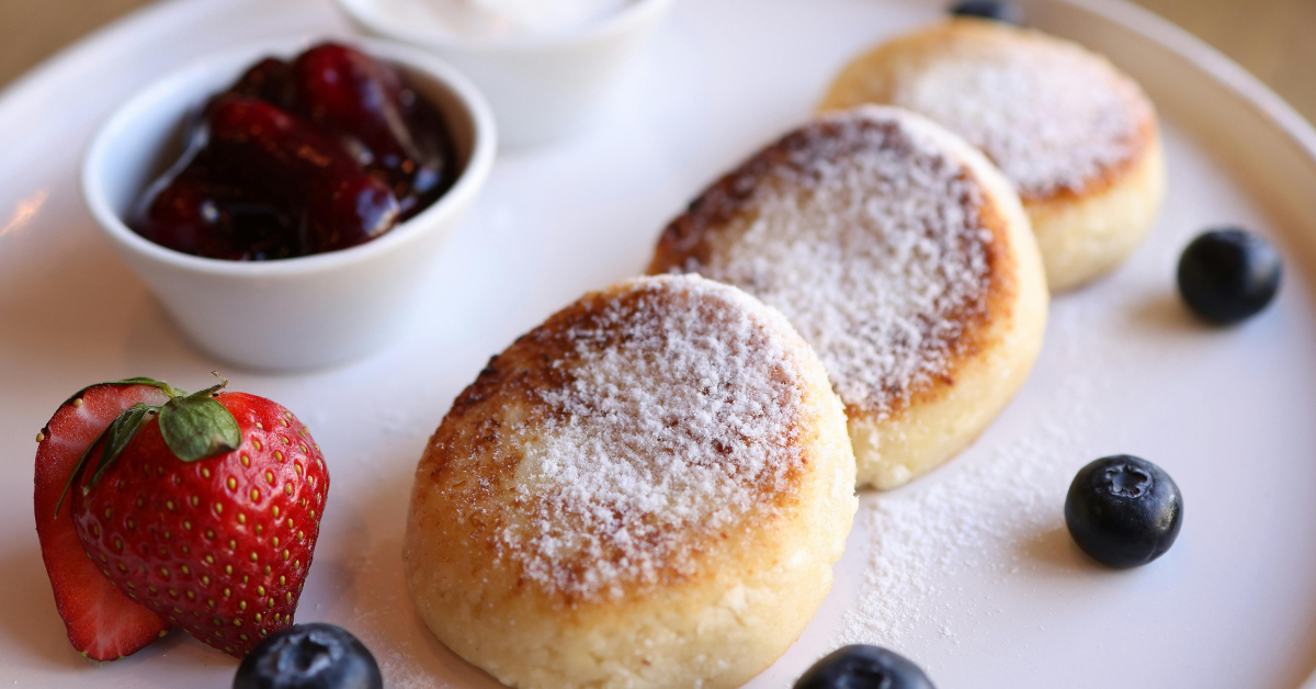 golden brown fluffy pancakes with blueberries and strawberries, sprinkled with powdered sugar
