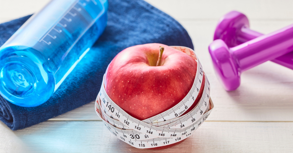 healthy snack like a red apple with a tape measure around it, a water bottle and small dumbbells